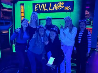 Members of the Munir Lab posing together while playing blacklight mini golf, standing in front of a glowing neon backdrop.