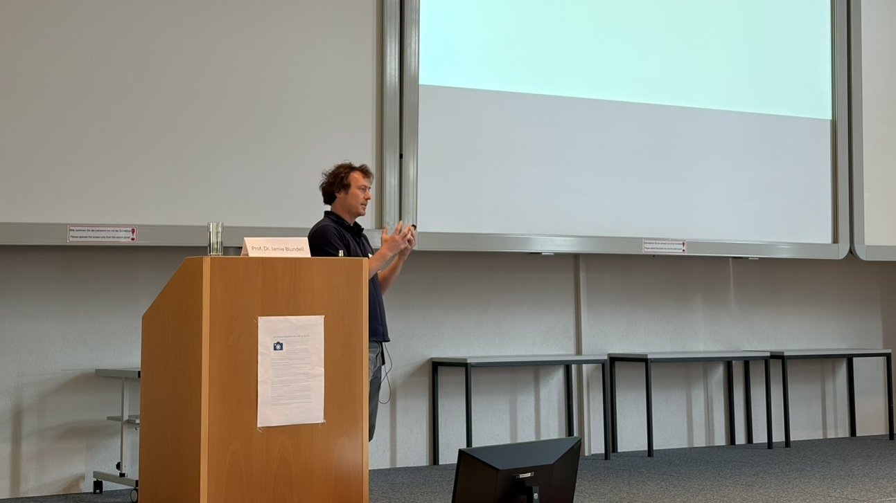 Prof. Dr. Jamie Blundell giving a presentation on stage during a scientific conference.
