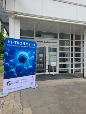 Entrance to the Hermann Staudinger lecture hall. Displayed outside the entrance is a large HI-TRON Mainz banner showing a blue scientific cell illustration.