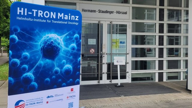 Entrance to the Hermann Staudinger lecture hall. Displayed outside the entrance is a large HI-TRON Mainz banner showing a blue scientific cell illustration.