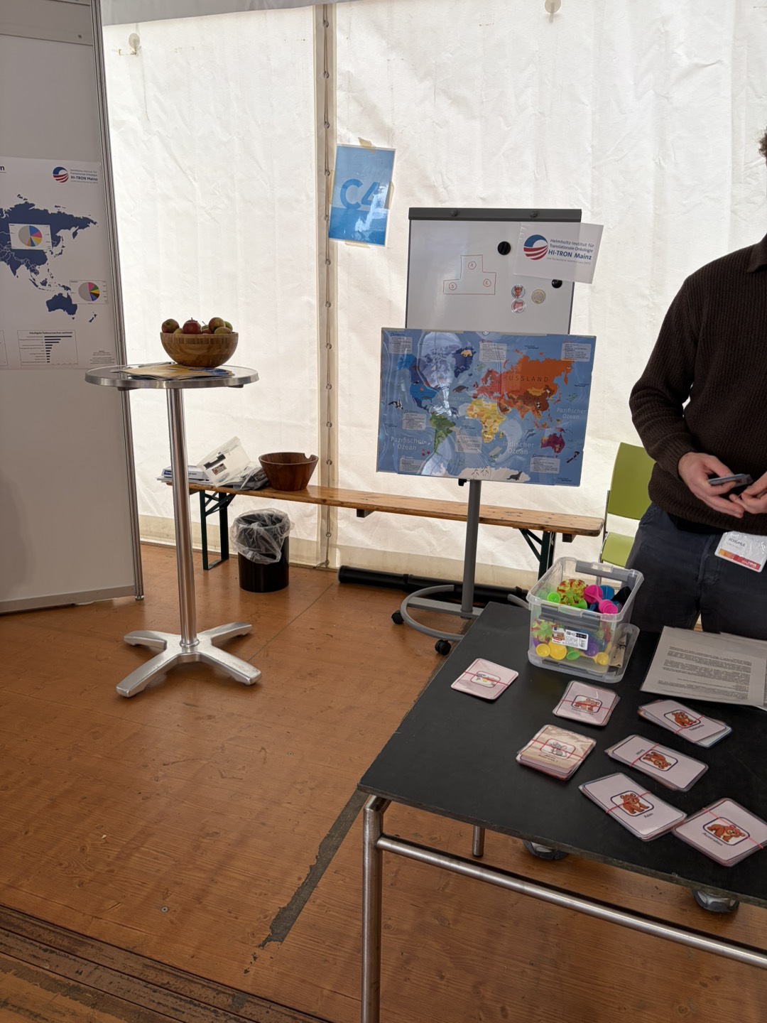 An exhibition booth featuring a world map, a fruit bowl, and a table with stacks of cards and educational materials.