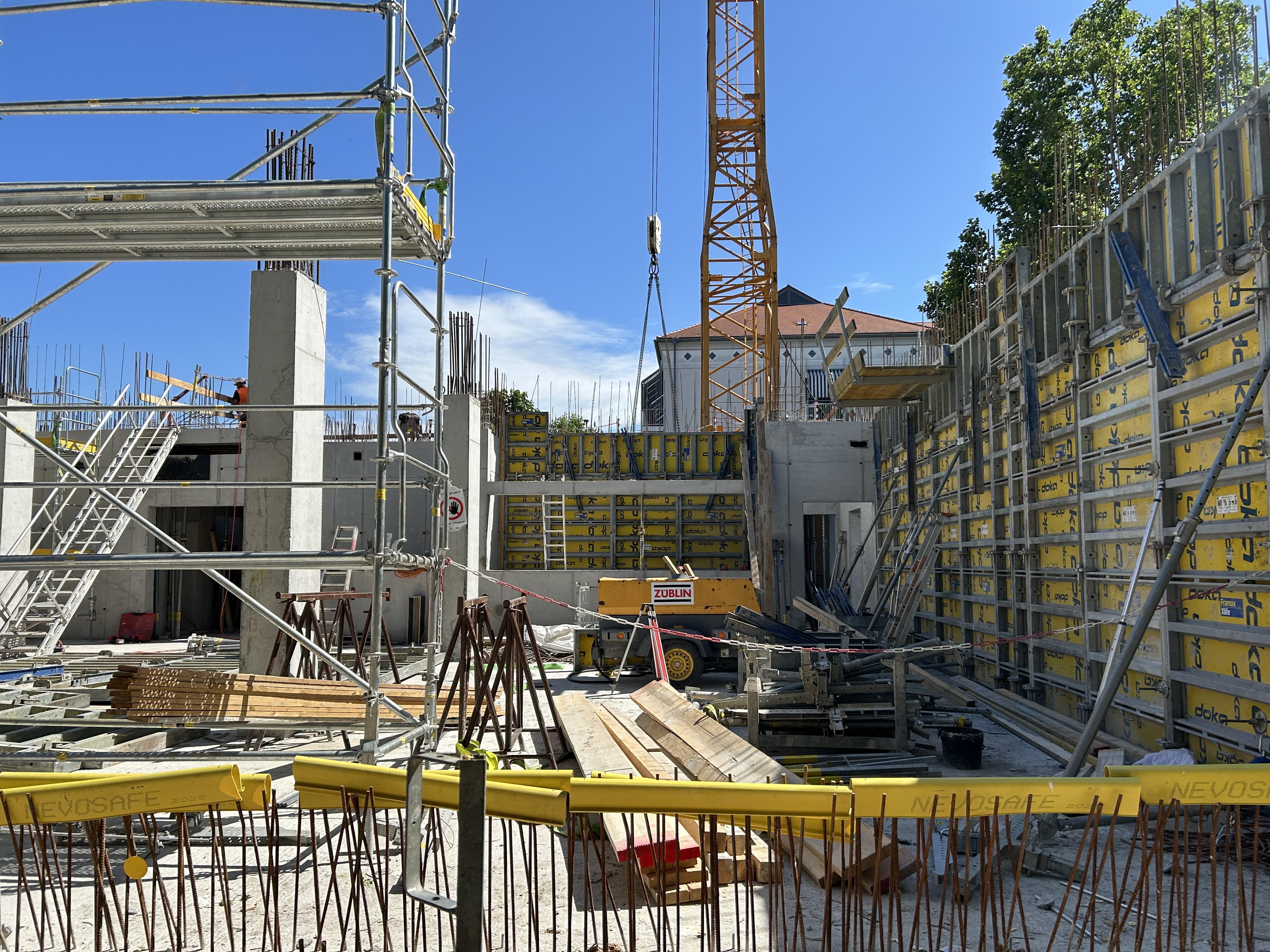 An active construction site with scaffolding, concrete columns, yellow formwork panels, and a crane, where workers are operating on multiple levels under clear blue skies.