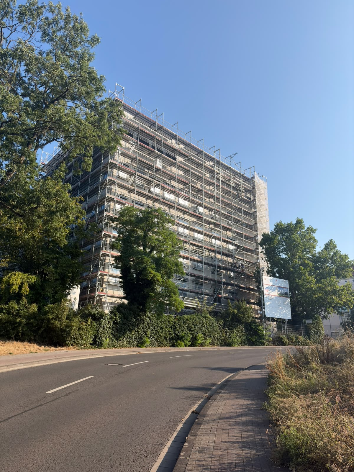 Photo of the new HI-TRON building under construction. Fully surrounded by scaffolding, with trees and a road in the foreground.