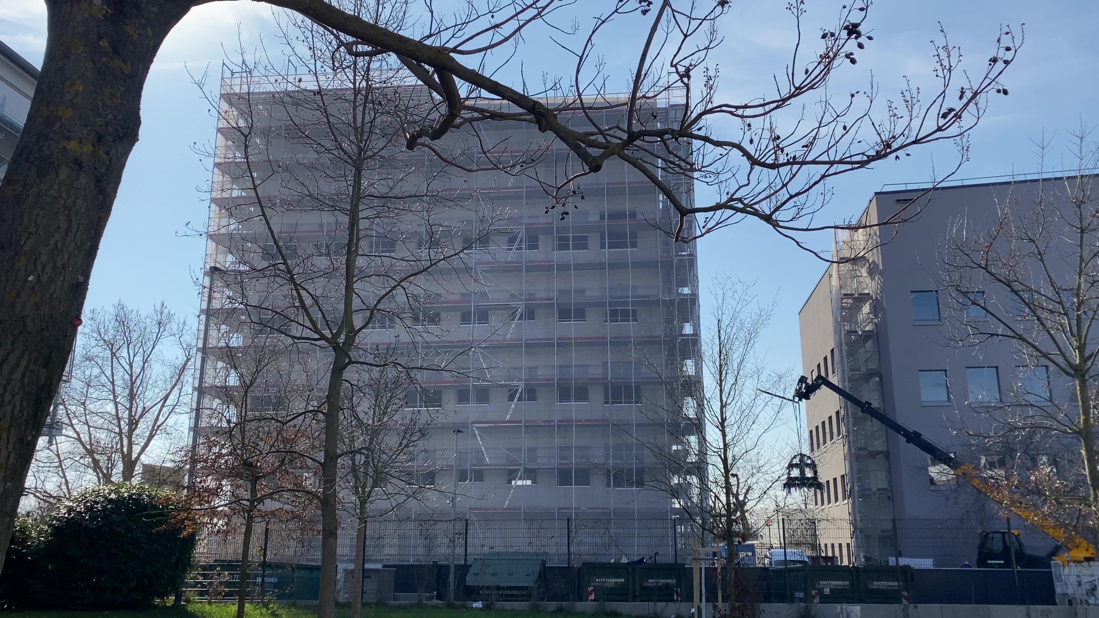 New HI-TRON building under construction covered in scaffolding, with a crane lifting a traditional topping-out wreath next to the site.