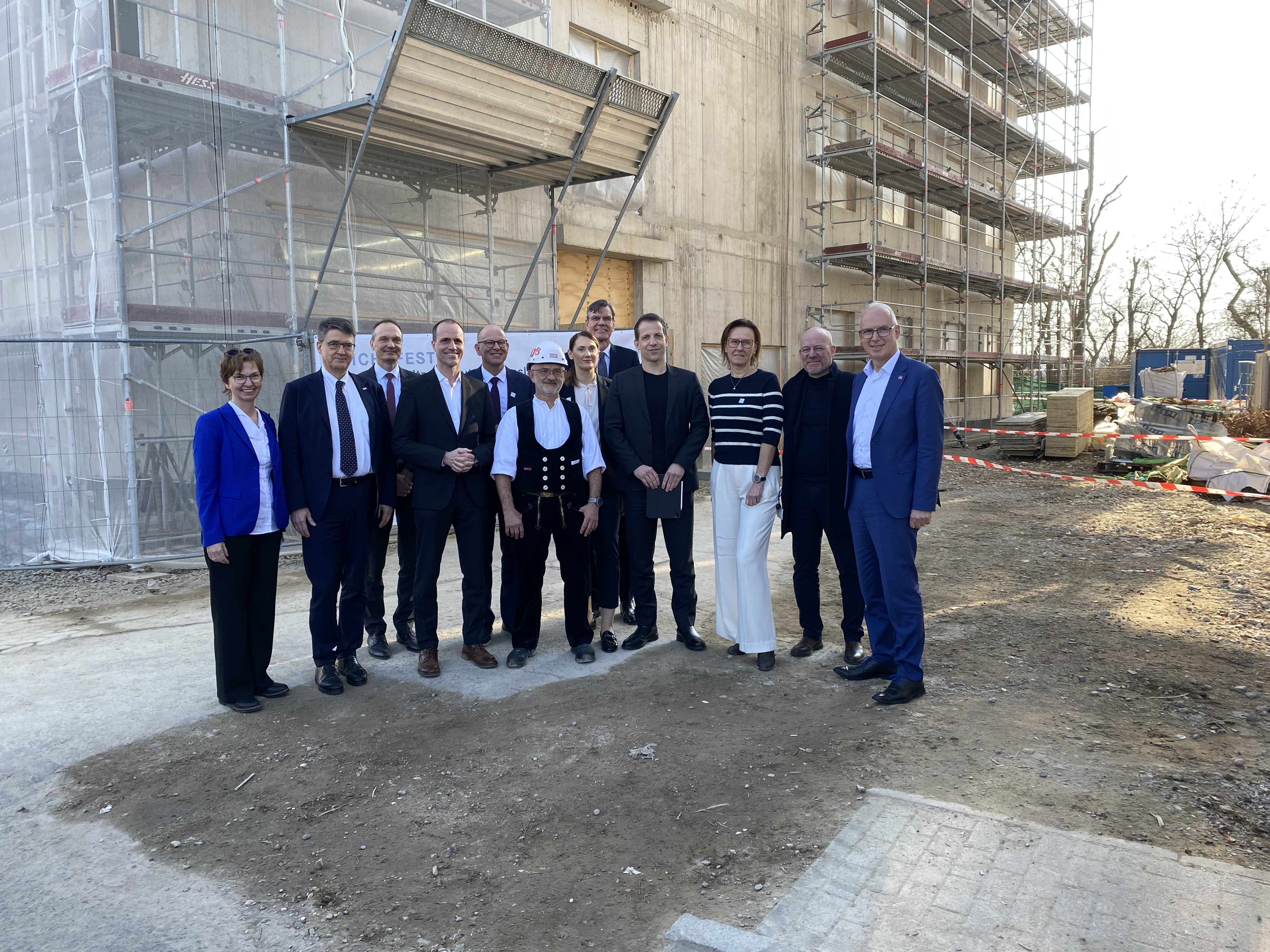 Group of officials, university leaders, and construction representatives standing at the construction site of the five-storey Helmholtz Institute for Translational Oncology in Mainz during the topping-out ceremony.