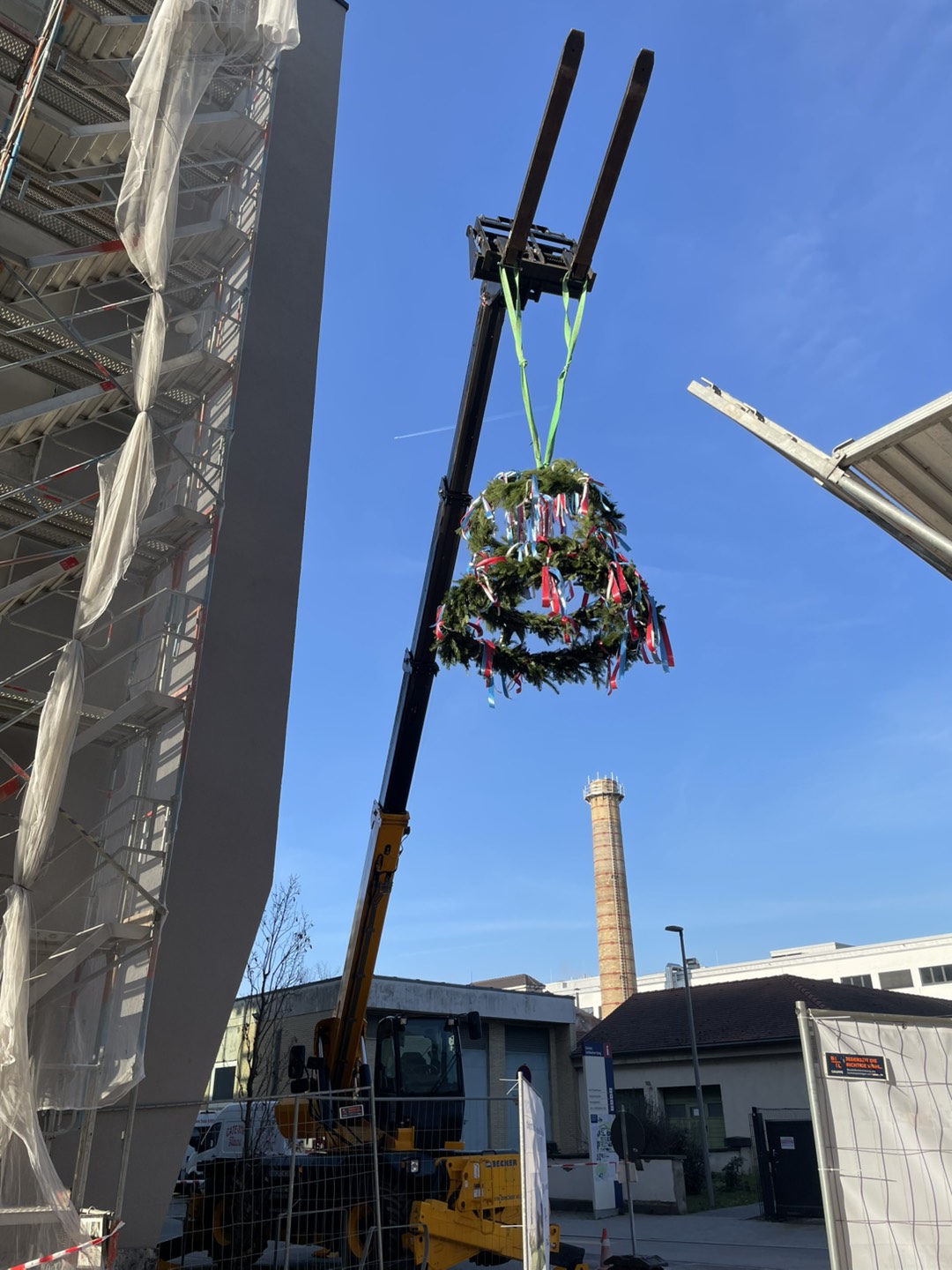 Construction crane lifting a traditional wreath with colorful ribbons during the topping-out ceremony at the building site of the new HI-TRON Mainz.