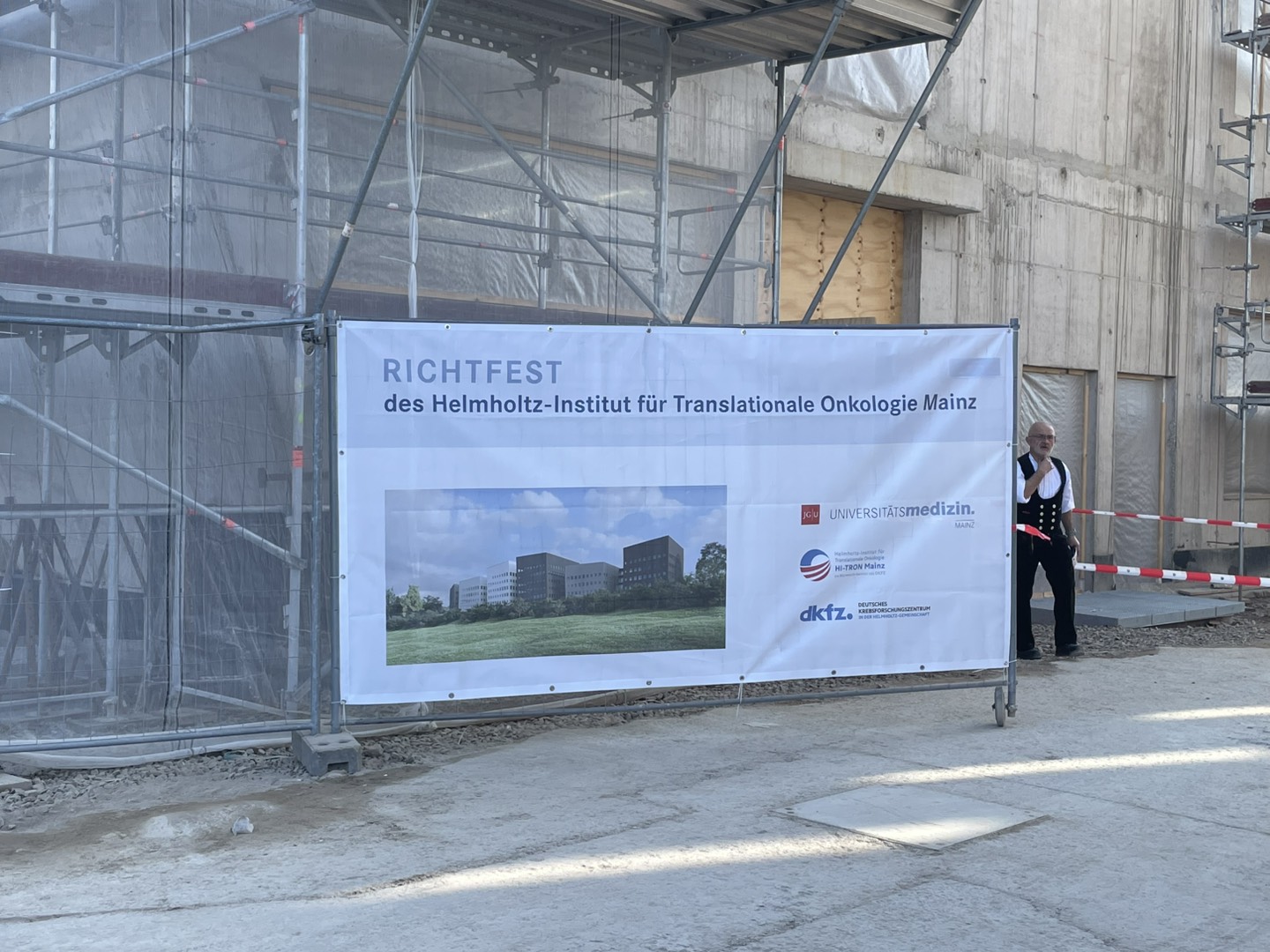 Construction site with scaffolding and a large banner announcing in German the topping-out ceremony of the Helmholtz Institute for Translational Oncology Mainz.