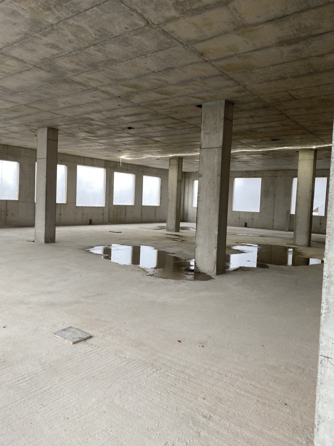 Interior of a concrete building under construction with support columns and puddles on the floor.
